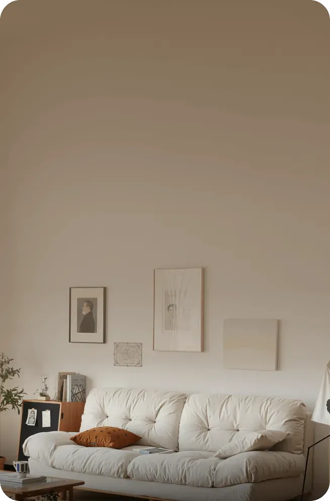 Cozy living room with a cream-colored tufted sofa, three framed artworks on the wall, and a small wooden table with books and plants.